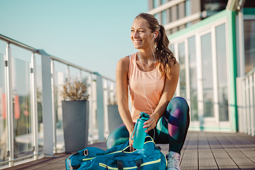 Smiling blond woman in the packing a bottle of water in her gym bag.