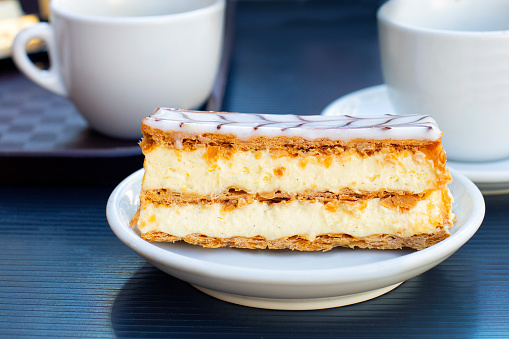 Eating traditional Millefeuille cake in one of French cafe. Thin layers of puff pastry and patissiere or custard vanilla cream. French dessert.