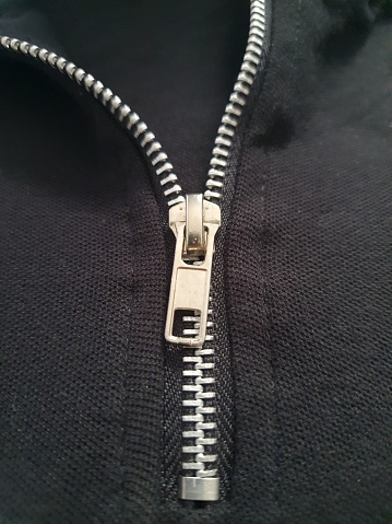 Close-up of chrome zipper, half open on a black background.