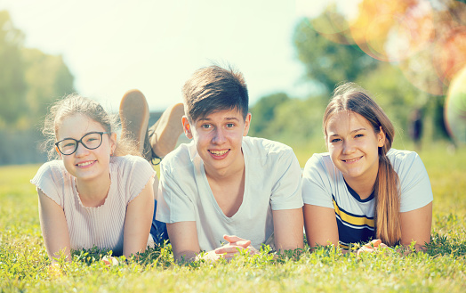 Portrait of teenagers lying on grass in park and looking happy