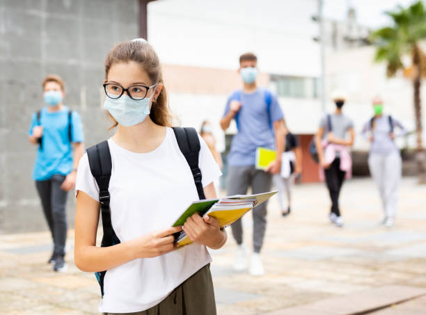 Teenage girl in protective mask with a backpack and notebooks walking in the street Teenage girl in a protective mask with a backpack and notebooks walking in the street 12 17 months stock pictures, royalty-free photos & images