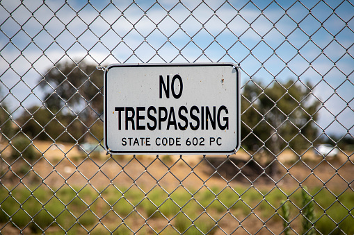 A sign stating No Trespassing on a chain link fence against a diffused background