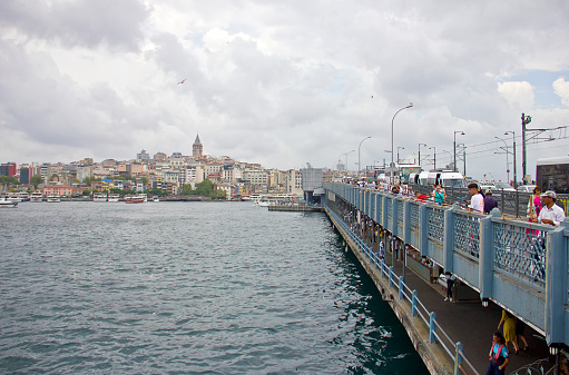 Istanbul,Turkey - August 10, 2022: Galata bridge linked eminönü and karaköy, there are lots of people on the bridge, lots of them are fishing, and beyond yhe bridge you see the galata tower in a cloudy summer day.