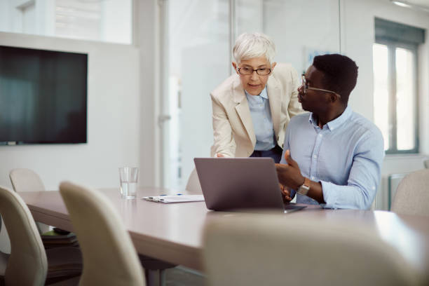 istock Mature CEO and her younger colleague talking while working on laptop in the office. 1416626898