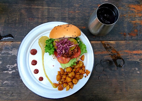 This is a photograph of a vegan BBQ burger made from jackfruit in a sloppy Joe style on a bun with roasted potatoes on the side, shot from an overhead view.