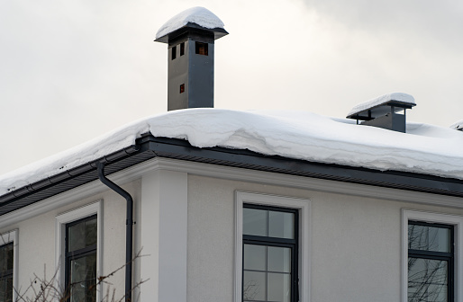Snow on green metal tiles roof of a european house with window
