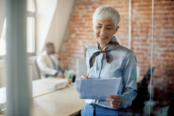 istock Happy mature businesswoman analyzing paperwork while working at corporate office. 1416627116