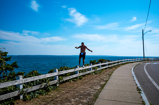 A man balancing along a guard rail high above the ocean in Falmouth on Cape Cod.