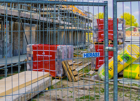 closeup of a fence in front of a construction site with building materials and house in background, construction site in Rucphen, The Netherlands, 6 may, 2022