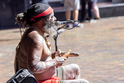 Sydney, Australia - August 21, 2022: Aboriginal male busker singing and performing with clapsticks at Circular Quay