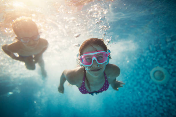 istock Two smiling kids wearing goggles swimming underwater in the swimming pool 1416634078