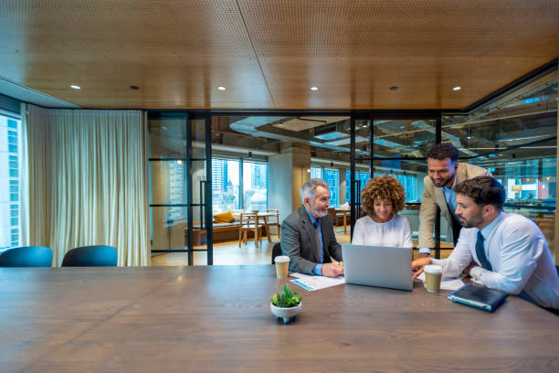 Four business people working on a laptop computer in an office conference room.