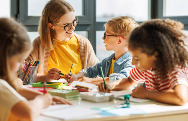 Teacher helping children with schoolwork Smart woman teacher in  glasses helping students to to schoolwork during lesson in light classroom at school business teaching student writing stock pictures, royalty-free photos & images