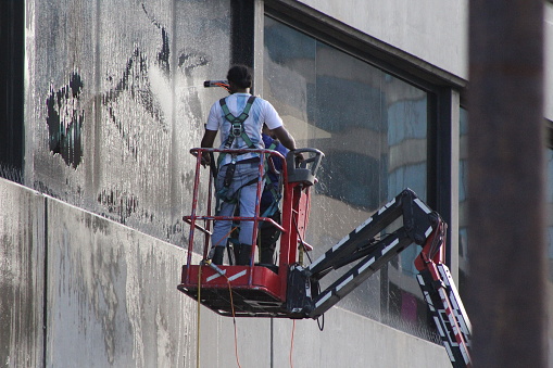 Port of Spain, Trinidad -July 24, 2022: 
Two window washers cleaning a  big window of a tall building  in the city