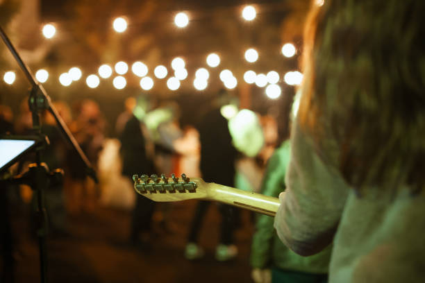 Rear view of the man sitting play acoustic guitar on the outdoor concert with a microphone stand in the front, musical concept.