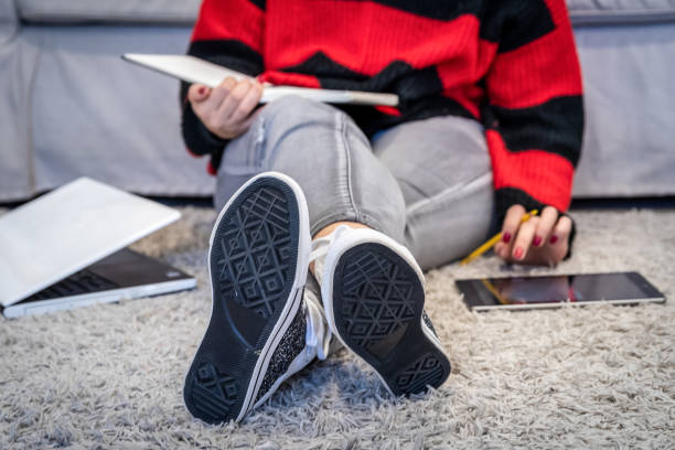Female drawing fashion design clothes into her sketchbook while learning from smart tablet