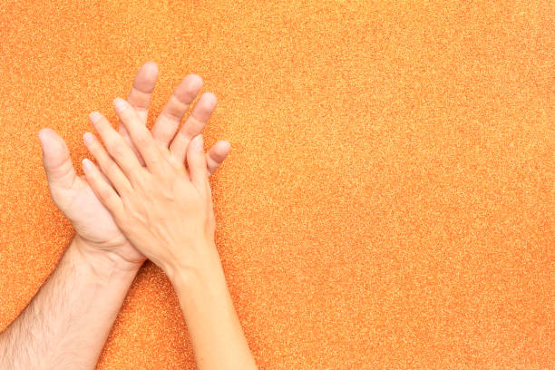 woman's hand resting on man's hand on bright orange background