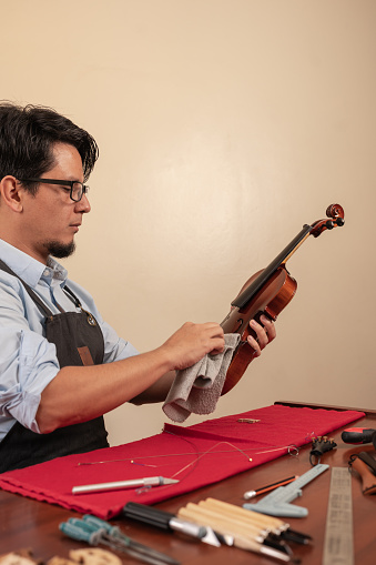Vertical photo of a worker cleaning a violin while repair it on a workshop