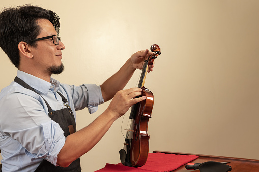 Profile of a male hispanic worker tuning a violin in a workshop