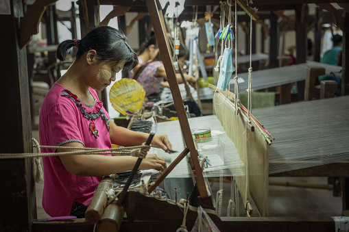 Amarapura, Mandalay, Myanmar, July 2022 - local Amarapura woman weaving hand-made tradional myanmar fabric at weaving factory