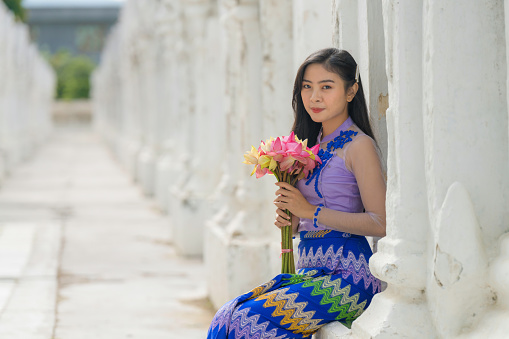 portrait of smiling Myanmar woman holding water lilly flower in Burmese traditional dress at Sandamuni pagoda in Mandalay