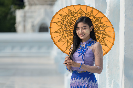portrait of smiling Myanmar woman with umbrella in Burmese traditional dress at Sandamuni pagoda in Mandalay