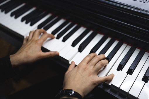 Unrecognizable elegant woman's hands playing piano indoor, with dark lighting