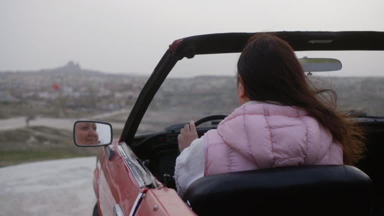 Woman is Sitting in her Red Retro Cabriolet Looking at Mirror, Rear View.