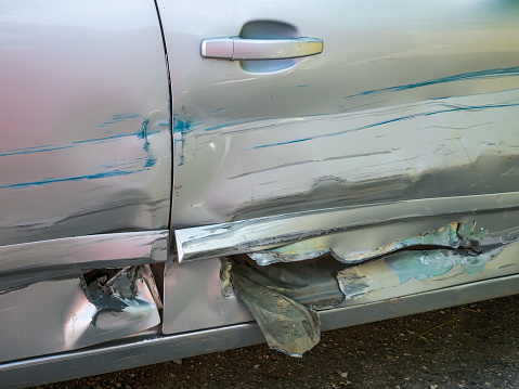 Silver colored car with scratches and extensive damage to the doors.