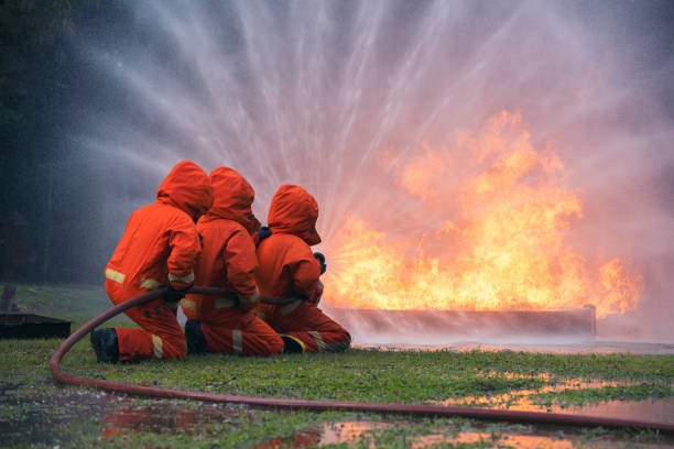 istock Firefighter Rescue team training in fire fighting extinguisher. Firefighter teamwork fighting with flame using fire hose chemical water foam spray engine. Fireman wear hard hat, safety suit uniform 1416790899