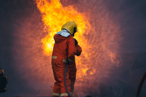 istock Firefighter fighting with flame using fire hose chemical water foam spray engine. Fireman wear hard hat, body safe suit uniform for protection. Rescue training in fire fighting extinguisher 1416790903