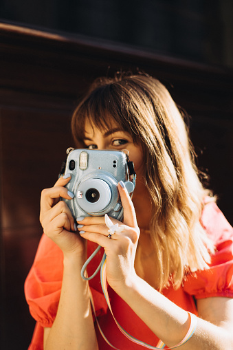 A portrait of a cute woman takes a shot on Instax camera, close up view