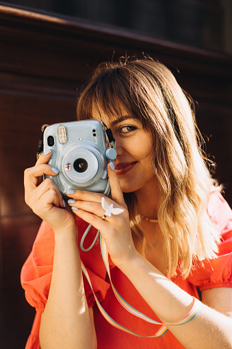 A portrait of a cute woman takes a shot on Instax camera, close up view