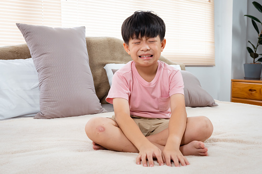Asian boy, wearing a pink T-shirt, Sit and cry and rub both eyes with both hands, He did so with regret, He did so with regret. , and he sat on the bed crying for a long time, frowning.