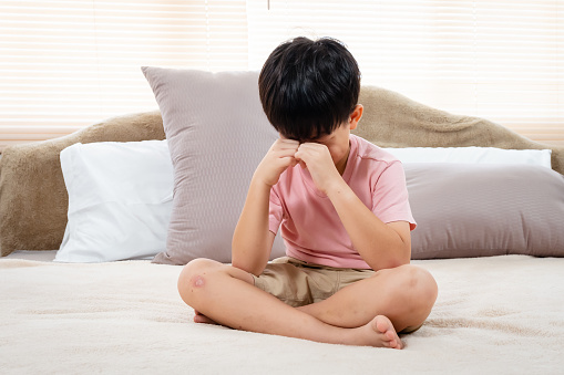 Asian boy, wearing a pink T-shirt, Sit and cry and rub both eyes with both hands, He did so with regret, He did so with regret, and he sat in bed crying for a long time.