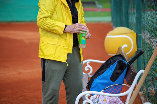 Senior man storing his tennis equipment in the bag because it's just about to start raining