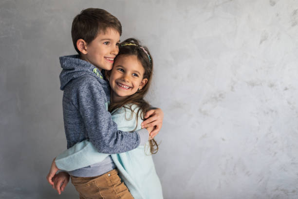 Smiling loving young boy and girl hugging. Portrait of them against grey wall. Copy space.