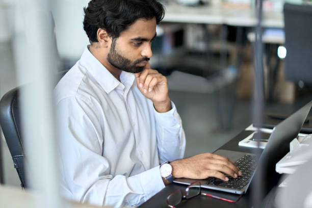 istock Busy young indian employee working on laptop, looking at computer in office. 1416817892