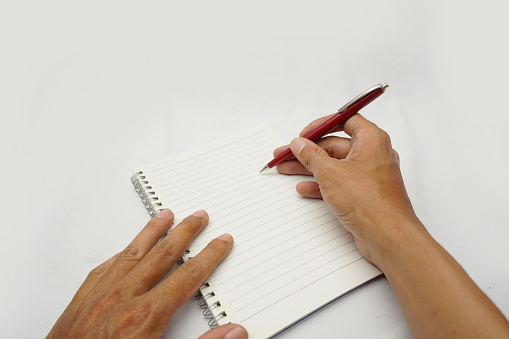 picture of asian male hand
holding a pen on a note book and preparing to write.
isolated on  white background.