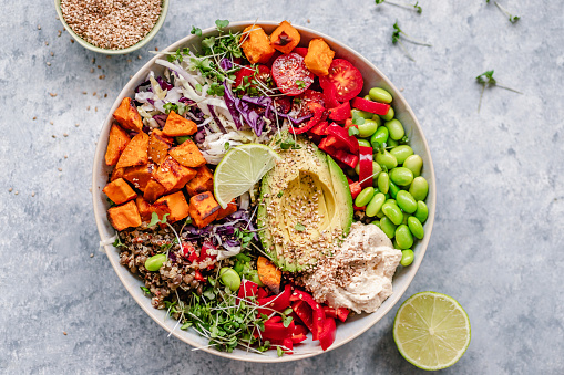 Overhead view of a colourful vegan bowl with quinoa, sweet potato, avocado, hummus and variety of veggies