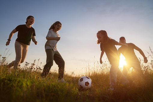 Happy family playing soccer. Young active people enjoying sunny summer evening outdoor. Healthy sport for kids. Football game club.