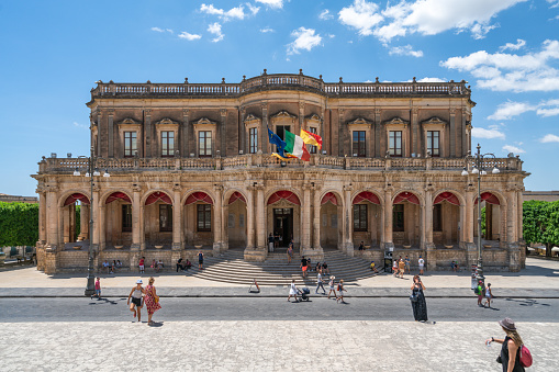 Noto, Sicily, Italy - July 9, 2022: Ducezio Palace, the town hall in Noto. A few people walking in front of town hall.