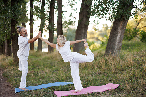 Young woman and her yoga instructor practicing stretching on a private yoga class in nature