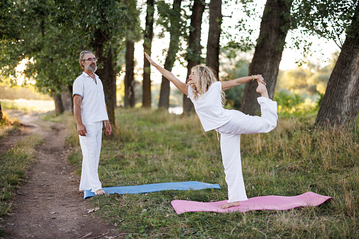 Young woman and her yoga instructor practicing stretching on a private yoga class in nature