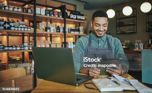 istock Smiling deli manager working on a tablet and laptop in his shop 1416830692