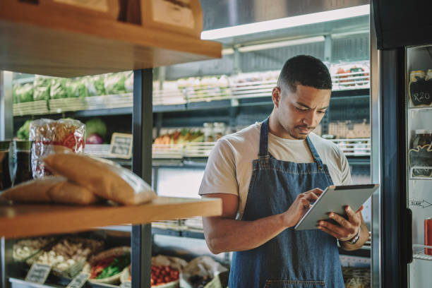Deli owner with a tablet checking inventory in his store stock photo