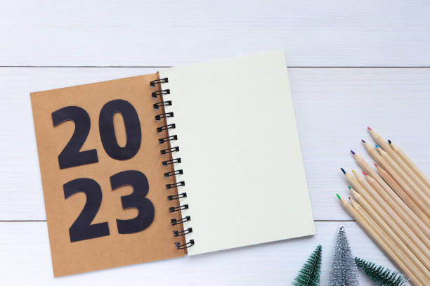 istock Happy new year 2023. 2023 resolutions list with notebook and colored pencils, christmas tree on white wooden table. Christmastime and new year celebration. Space for text. 1416833521