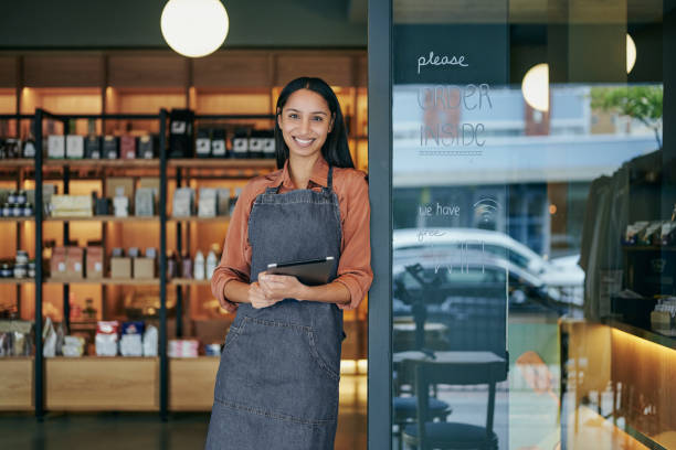 Smiling deli owner standing with at tablet at the door of her shop stock photo