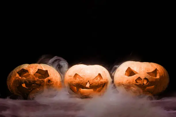 Photo of Orange Jack o' Lantern with smoke on black background. Halloween pumpkin with lights and creeping smoke