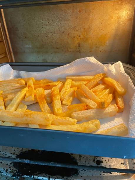 istock Image of baking tray lined with greaseproof parchment paper containing freshly cooked crispy homemade French fries on hot oven shelf, focus on foreground 1416848723
